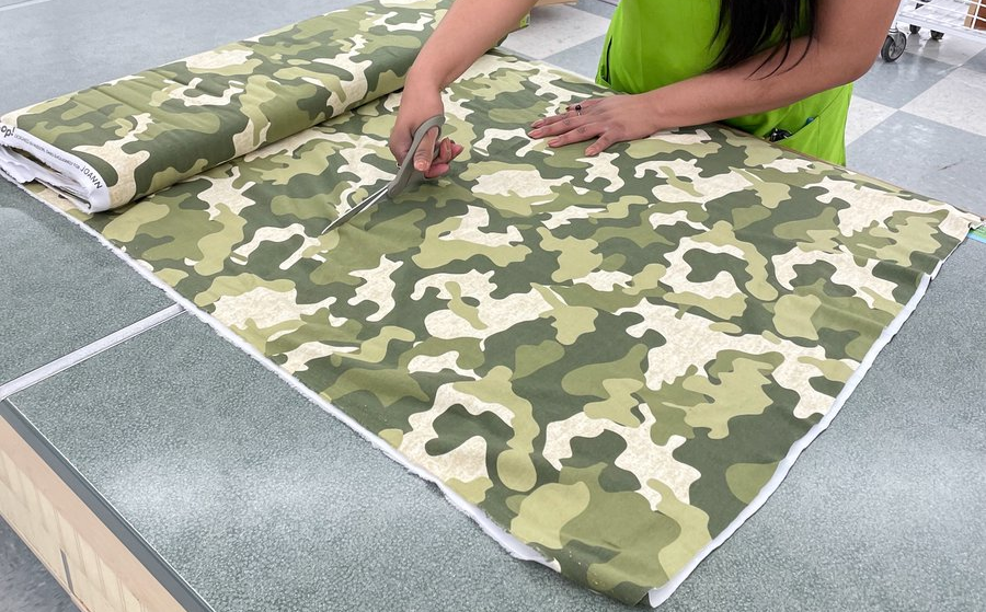 Picture of an employee from Joann Fabrics cutting camouflage fabric with a pair of scissors.
