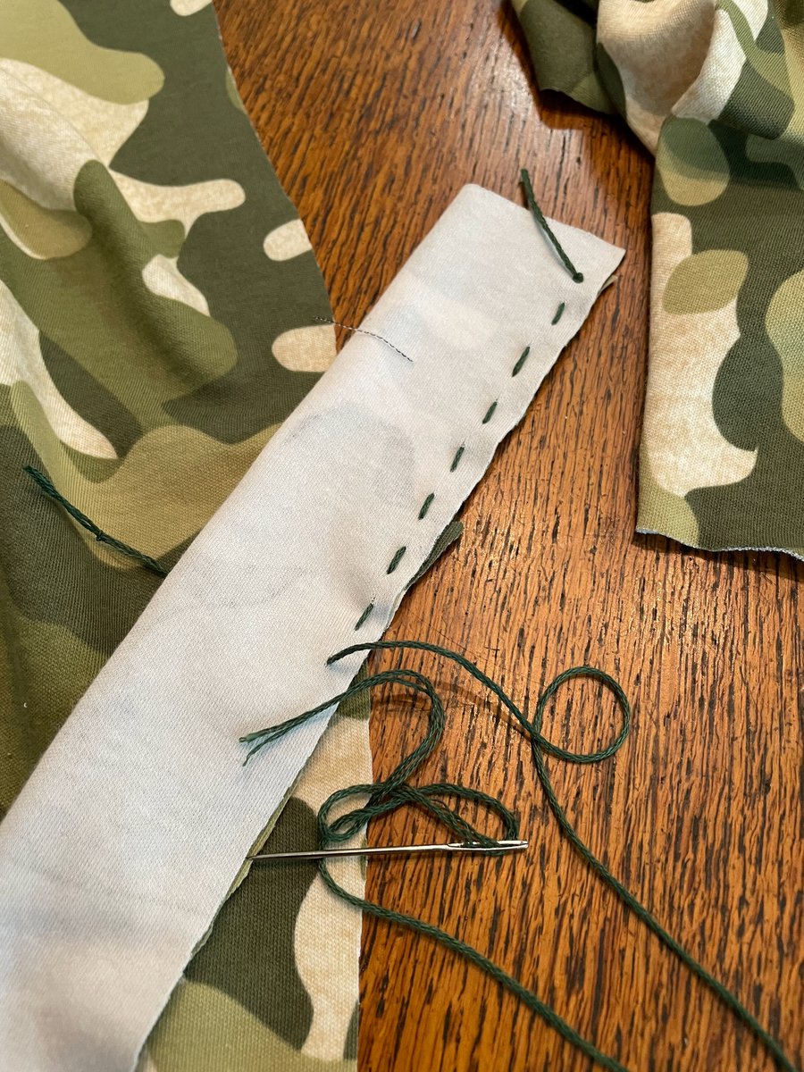 Picture of camouflage fabric, a sewing needle, and stitches with green thread.